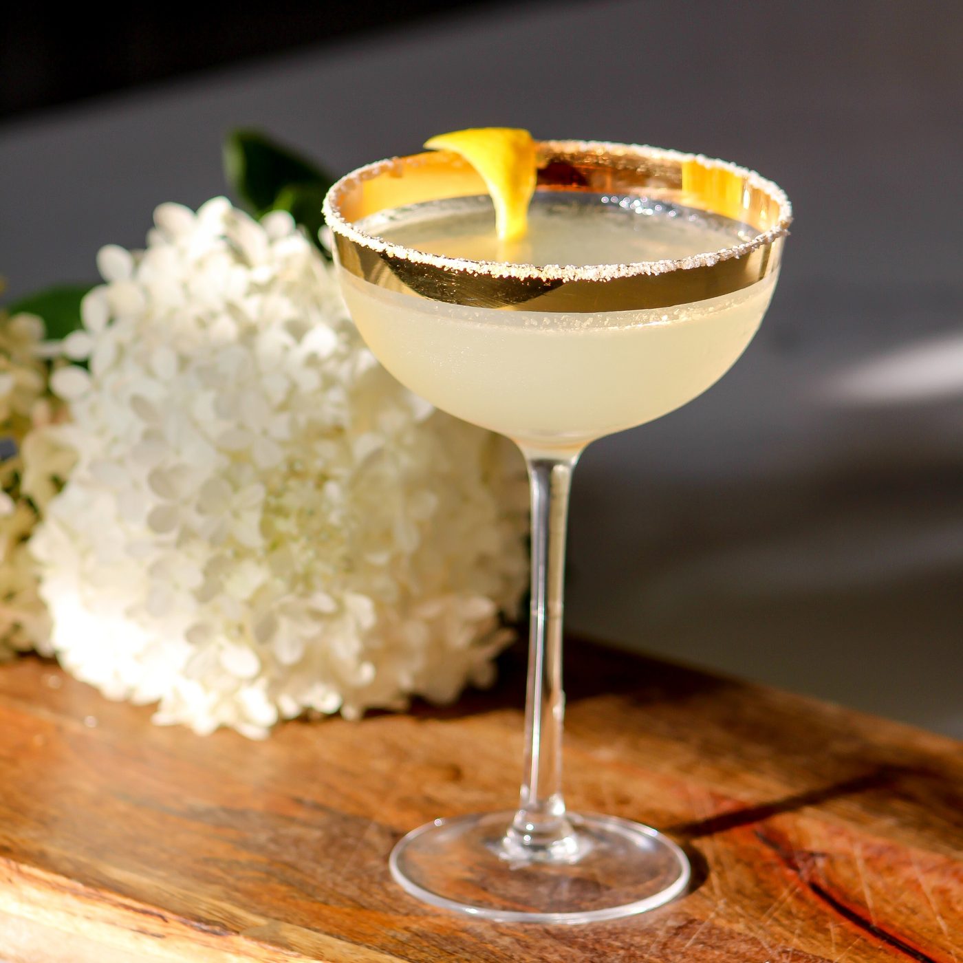 Craft cocktail with an orange twist garnish, floral backdrop
